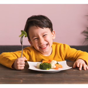 child holding up a fork with broccoli on it and smiling