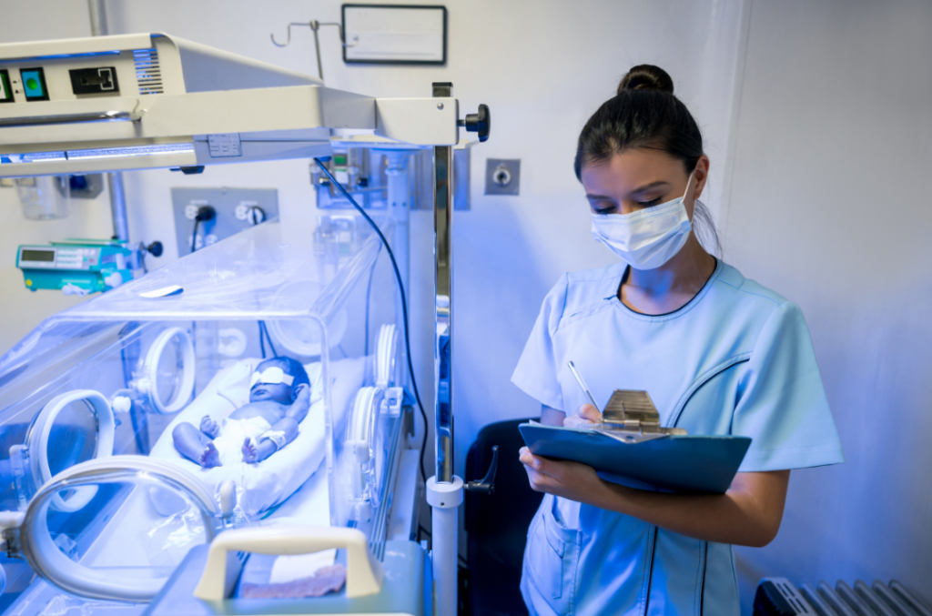 baby in an incubator with a nurse taking notes on a clipboard beside him or her
