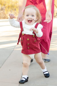 a child with blond hair and a feeding tube smiling while walking in front of their mom