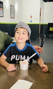 boy (Julian) smiling while sitting at a table with a bowl of ice cream in front of him