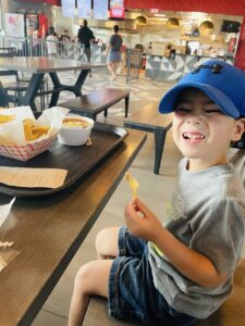 child wearing a blue hat, smiling while sitting at the table with fries